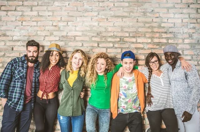 A diverse group of young people standing together against a brick wall, smiling.